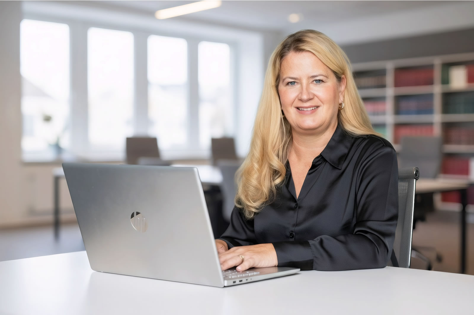 Hochwertige Bildaufnahme einer professionellen Anwältin in einem modernen Büro mit Laptop, die Kompetenz und Vertrauen ausstrahlt.